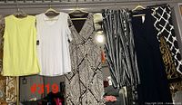 Five garments hanging: yellow top, white top, brown geometric dress, striped pants, black dress