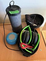 Overall lot showing tall Bluetooth speaker, blue mini speaker, foldable headphones in case, and sleep headband headphones pouch