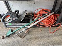 Hedge trimmer, extension cord and two long-handled garden tools on shelf