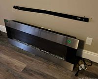 Front view of electric fireplace insert leaning against wall with mounting bracket above and power cord visible