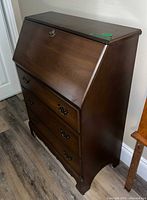 Closed view of dark brown Krug drop-front secretary desk showing three drawers and brass pulls
