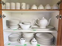 Cabinet view showing stacked plates, bowls, mugs, saucers, gravy boat on platter, teapot