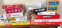 Stacked board games showing titles including Yahtzee, Trivial Pursuit, Mad Gab, Whatzit?, Payday, Ratrace, Beat The Parents, Mouse Trap, Monopoly