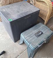 Large black deck box and smaller green toolbox seat side by side