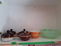 Group view of jadeite bowl, Pyrex bowl, and five lidded French onion soup bowls in cabinet