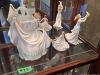 Group of Royal Doulton figurines displayed on glass shelf