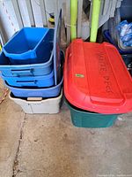 Stack of four nested blue/grey totes beside green tote with red lid