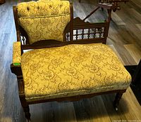 Front angled view showing tufted back, floral upholstery, carved frame, casters