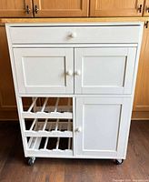 Front view of white kitchen cart showing drawer, cabinet doors, wine racks, wood top and casters