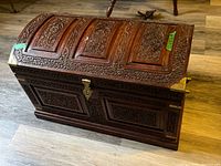 Full view of carved wooden trunk closed, showing domed lid and brass hardware