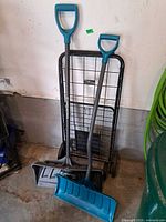 Two Yardworks snow shovels and Easy Wheels folding cart standing together