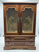 front view of wooden jewelry cabinet showing glass doors and drawers
