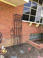 Three black metal trellises and metal candle holder stake arranged outside against a brick wall showing overall condition.