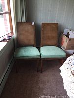Two ridgeway dining chairs with green upholstered seats and cane backs positioned side by side, showing some wear, scratches, and chips on legs.