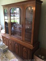 Front view of the wooden china cabinet showcasing three glass doors for display with visible shelves inside and lower cabinet doors and drawers with hardware.