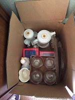 Photo of assorted porcelain tea set, glass drinking glasses in box, glass platters, and small decorative kitchen items.