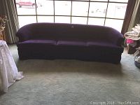 Front view of the three-seat purple curved sofa showing the full length, fabric upholstery, and shape.