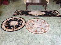 Photo showing the black runner and two round rugs on carpeted floor, one round rug matching runner design, the other green with floral pattern.