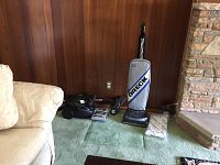 Both vacuums shown side by side on carpet against wood paneling, Oreck upright and Electrolux canister.