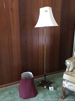 Full view of floor lamp with white lampshade in front of wood-paneled wall, showing overall condition and height.