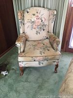 Front view of the wing back chair showing the full chair including floral upholstery and wooden legs.