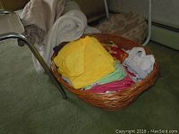 Photo of large woven basket filled with various folded linens, towel, and pillow