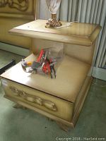 Single nightstand showing carved decorative front on drawer, stained top surface with edge wear.