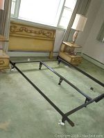 Wooden queen size headboard with carved decorative design, flanked by nightstands, attached to black adjustable metal bed frame