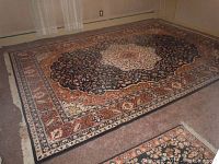Large area rug with black background and floral medallion pattern laid flat on floor