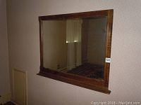 Full view of the rectangular wall mirror with wooden frame hung on wall, showing reflection and room behind.