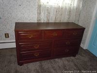Front view of a wooden dresser with 3 small drawers on top and 4 larger drawers beneath, gold drawer handles, placed on carpet flooring.