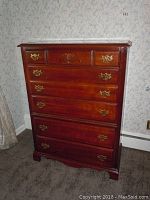 Full view of wooden dresser with five drawers against wallpapered wall.