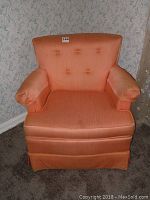 Front view of peach upholstered armchair with button tufted backrest and armrest covers showing stains and general wear