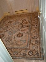 Full view of large rectangular area rug in a room against wall and curtain showing full patterned design.