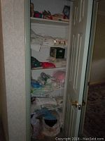 Closet with multiple shelves holding folded linens, towels, stuffed animals, and bags containing cleaning items.