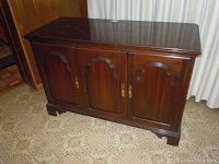 Front view of the dark wood media cabinet showing three paneled arched doors and brass handles.