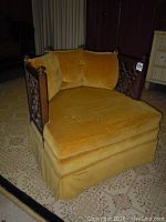 Side angle of the vintage club chair showing gold velvet upholstery and intricate carved wood panel on the side.