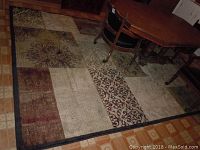 Full view of the black and gray patchwork area rug with a chair and table partially on it showing various patterned rectangular patches.