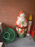 Santa Claus figure standing next to two green metal tree stands and Noel candle decoration.