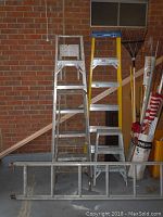 Five ladders leaning against a brick wall showing a 6 ft aluminum Werner step ladder, 4 ft wooden step ladder, 2 ft aluminum step ladder, 10 ft aluminum extension ladder, and an additional 6 ft aluminum step ladder.