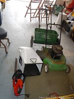 Gas lawn mower, Scotts spreader, grass catcher, hedge trimmer, and hoses shown on floor.