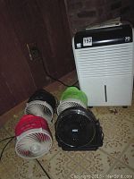 Kenmore dehumidifier standing with four 10-inch portable fans in red, black, green, and black (HDX brand) in front on linoleum floor