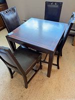 Square wood dining table with three chairs around it