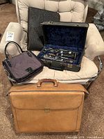 Group shot of briefcase, nylon handbag, clarinet in case and chair