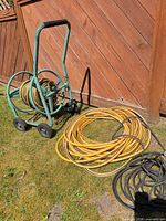 Full view of hose reel cart with coiled yellow hose, loose yellow hose coil, black hose on grass