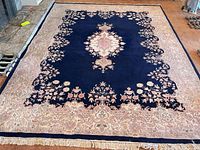 Full view of hand-knotted Persian-style wool area rug showing navy field, floral border, central medallion, fringe