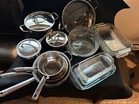 Assortment of stainless pots, pans with lids and stacked Pyrex glassware