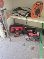 Shelved tools including framing square, extension cord reel, Milwaukee bag, sander, jigsaw, cords