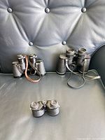 All three binoculars displayed on chair: Brookstone compact front, International left, Fisher-Dietz right