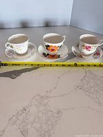 Three floral bone china teacups with saucers, ruler for scale